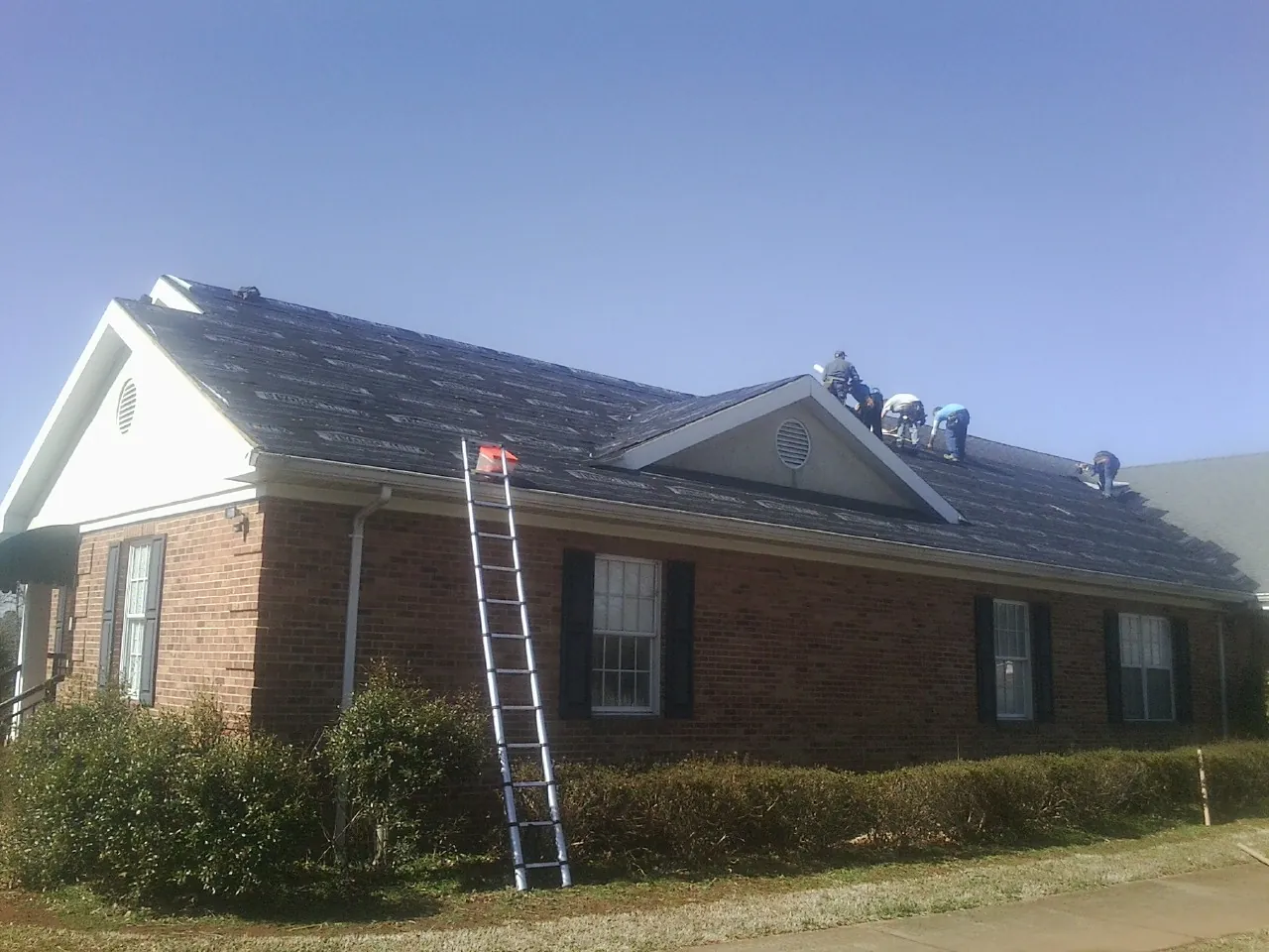Crew tearing shingles off a brick ranch roof with a ladder set — Emergency Roof Repair work by our crew in Berne