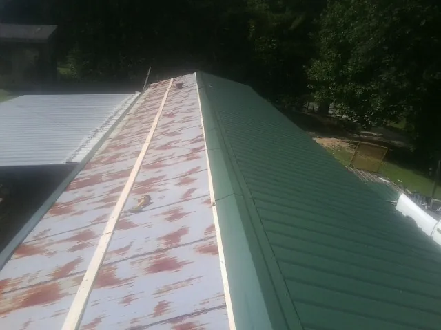 Old rusted panels beside newly installed green metal roofing — Wind Damage Roof Repair by Roofing Brothers in Berne