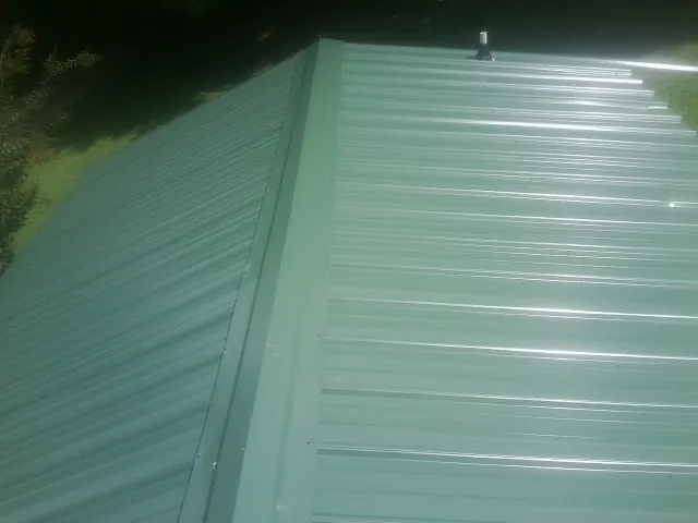 New green metal panels meeting at the ridge of a roof — Flat Roof Repair work by our crew in Berne