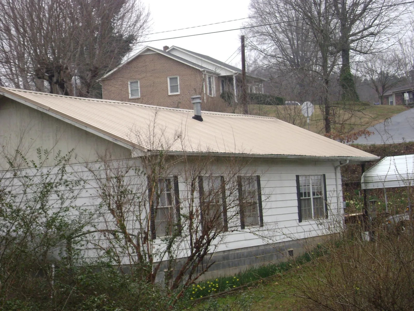 Tan metal roof on a white sided house set into a hillside — Commercial Roofing by Roofing Brothers in Berne