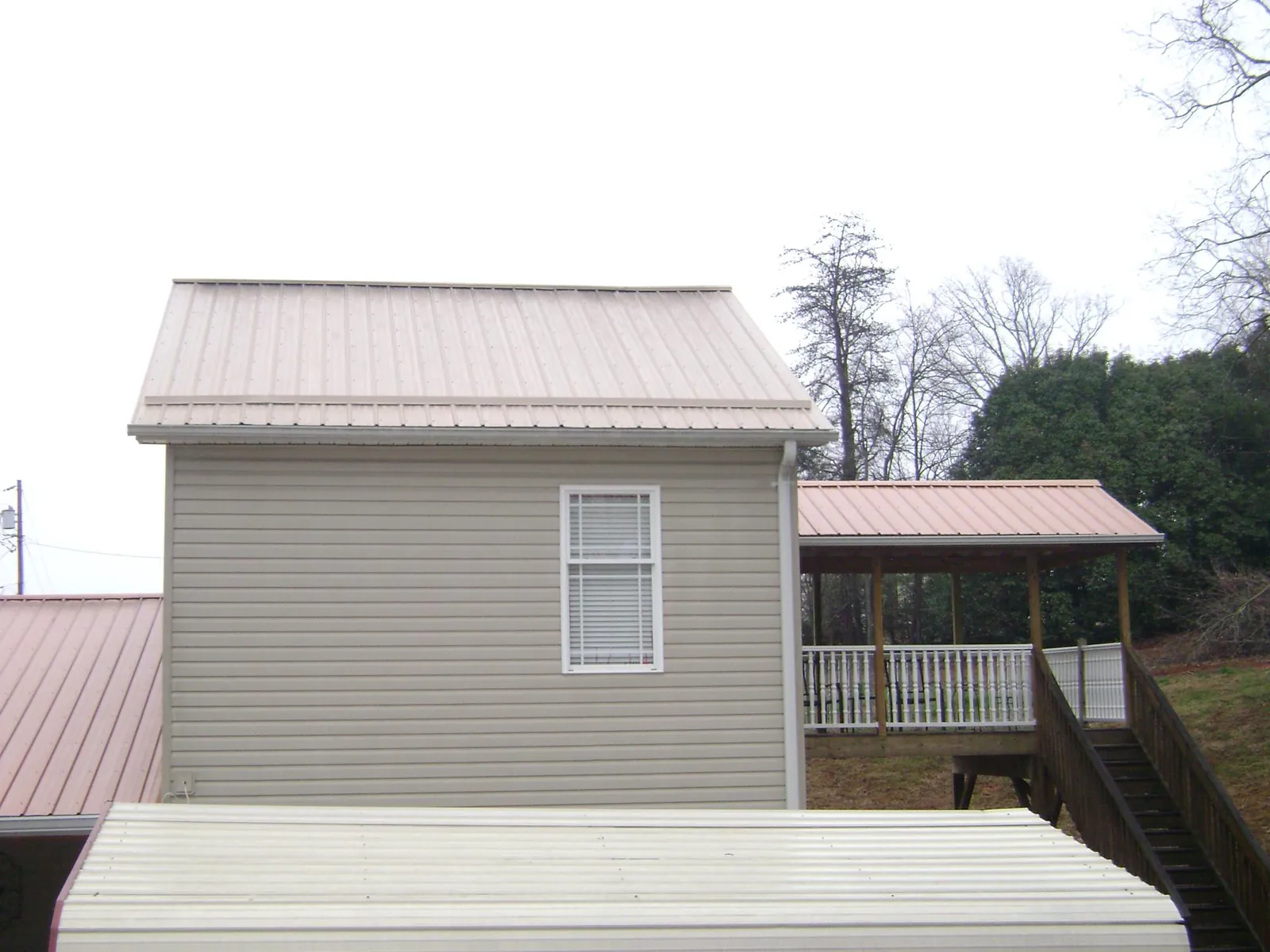 Tan metal roofs on a two story addition and attached porch, from a Roof Replacement job in Berne